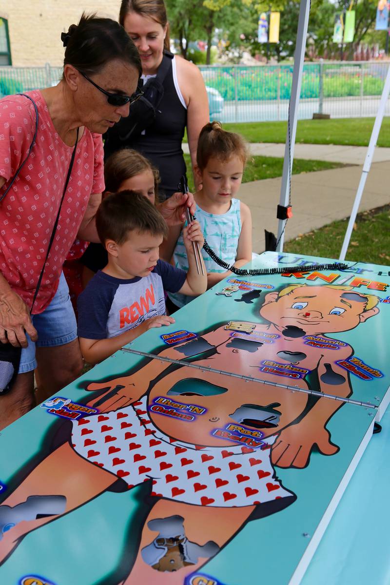 Susan Welsh helps 3-year old Tommy Calabrese with a game, while Sarah Calabrese, Leah DeLeon and Brie Calabrese look on at the annual Batavia Windmill City Festival on Saturday, July 12, 2025.