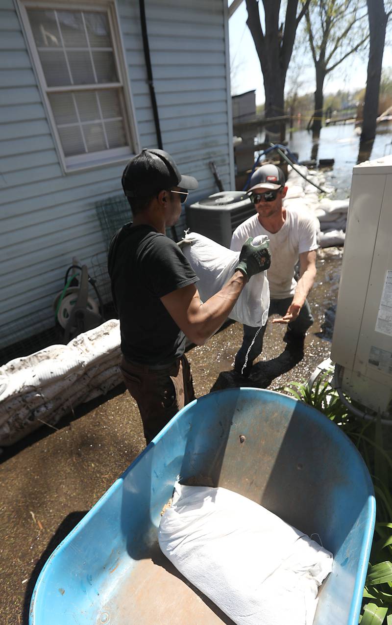 Jai Hale hands a sandbag to Ryan Downey as the works to sandbag Downey’s home with McHenry Home Depot volunteers as flooding continues on the Fox River on Wednesday, April 22, 2026, near Burton’s Bridge.