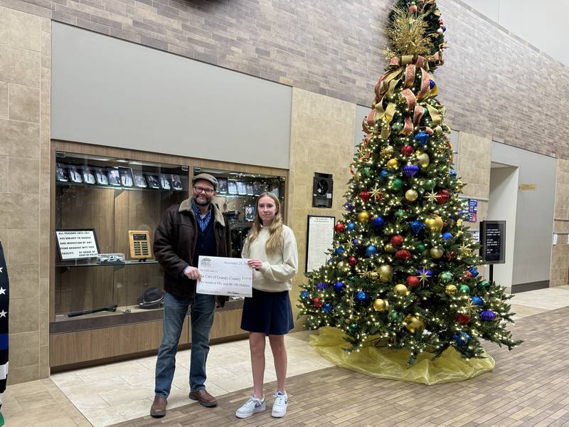 Adeline K., right, hands a check to Eric Fisher of We Care of Grundy County.
