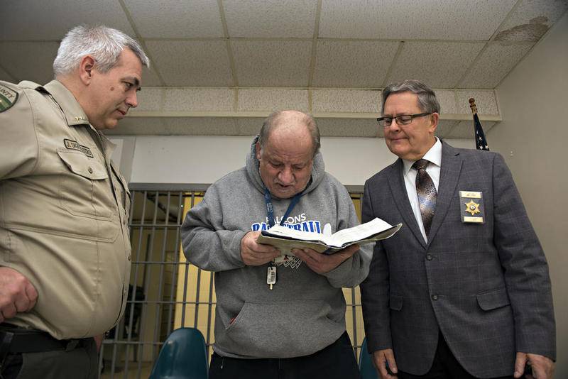 "Bible  Joe," as Shoemaker is known, reads a passage Wednesday after being recognized for four decades volunteering at the Lee County Jail. Jail Administrator Jack Skrogstad (left) and Chaplain James Stroup celebrated the work with Joe.
