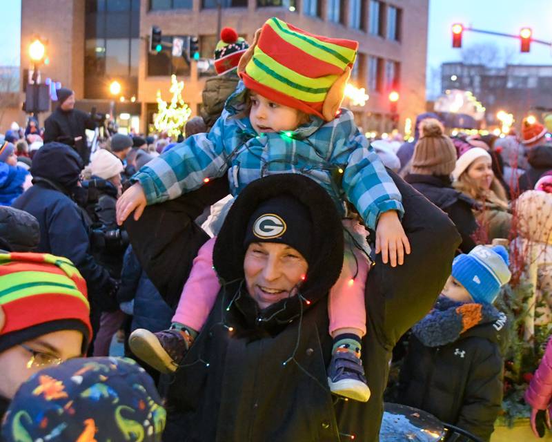 Glen Williams, grandpa, holds Winry Williams, 2, of Downers Grove while wearing Christmas lights as they attend the Christmas tree lighting ceremony on Friday Nov. 29, 2024, in downtown Downers Grove.