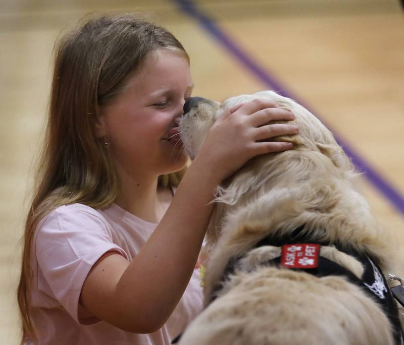McHenry Police Department therapy dog, Oakley, gives Elise Schift, the daughter teacher Emily Schilf, a kiss on Friday, Aug. 16, 2024, at Duker Elementary School after a ceremony to present Oakley with a patch in honor of her mother, who passed away earlier in the year.