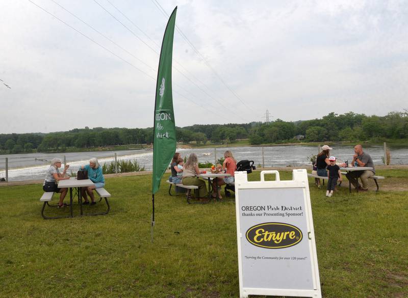 People sit at picnic tables overlooking the Rock River at the River's Edge Farmers Market on Thursday, June 5, 2025. The markets are held each Thursday night from 5-7:30 p.m. at 123 N. 2nd St., along the riverfront below the Oregon dam on the west bank of the Rock River. The weekly events also include music, kids activities, and food booths.