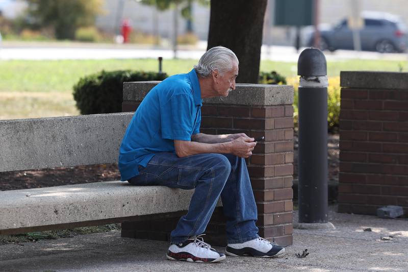 A man checks his phone while sitting in the shade on Thursday, Sept. 12, 2024 in downtown Joliet.
