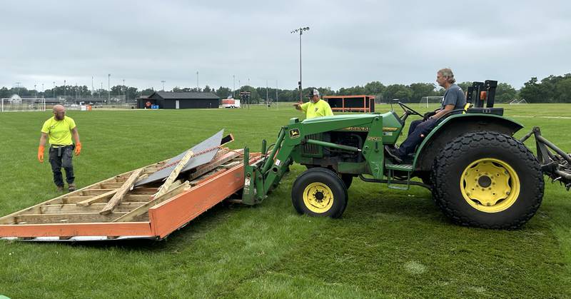Byron School District employees Nick Sapoznick, Jim Getzelman, and Terry Wilken remove one of the wooden team shelters from the high school soccer field on Tuesday, July 16, 2024.