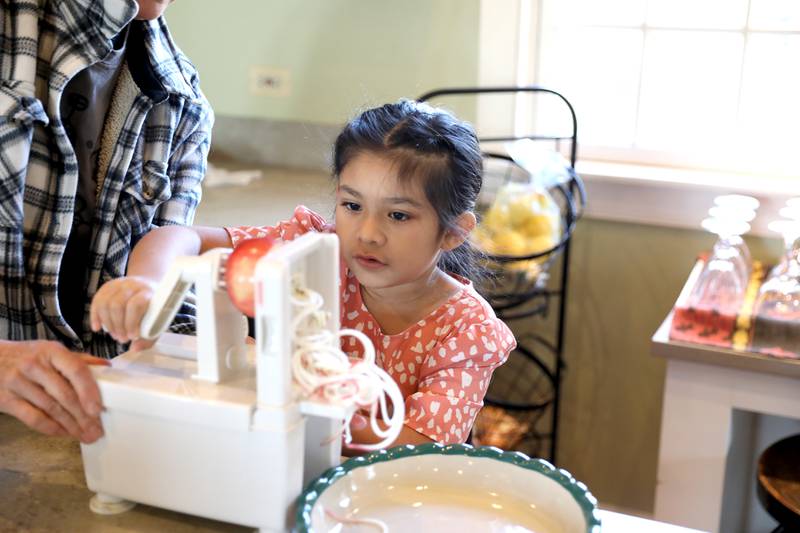 The Learning Door student Gracie Latigo, 7, spiralizes an apple with the help of Farmhouse School owner Leslie Meredith during a Fun Friday at the Farmhouse School in Campton Hills.