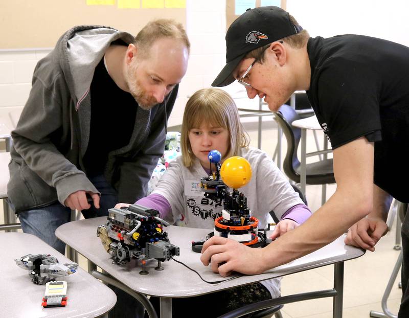 Nelora Squire, 10, from DeKalb, along with her dad Steve (left) learn about how engines works Saturday, April 5, 2025, from Ben Charbonneau, a junior in the Barb Brick Club at DeKalb High School. Squire was attending  Meta’s Barb STEAMCon at DeKalb High School. The event featured sessions focusing on the areas of science, technology, engineering, arts and math.