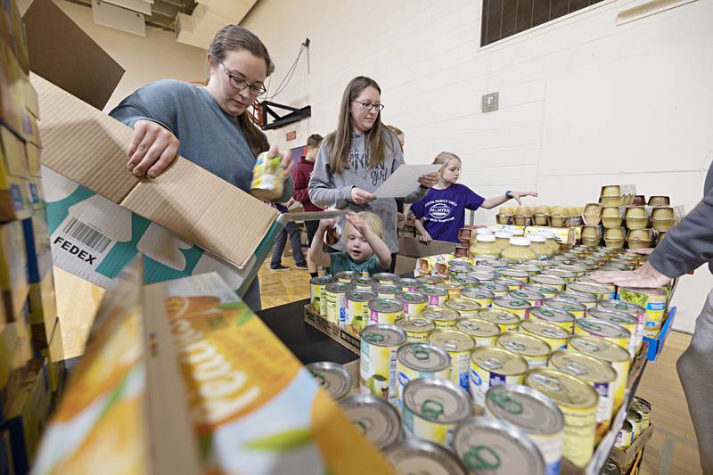 Hadley Wagner, 4, helps Megan Hummel (left) and Ashley Noble load food items into a box Tuesday, Dec. 20, 2022 at the Dixon YMCA.
