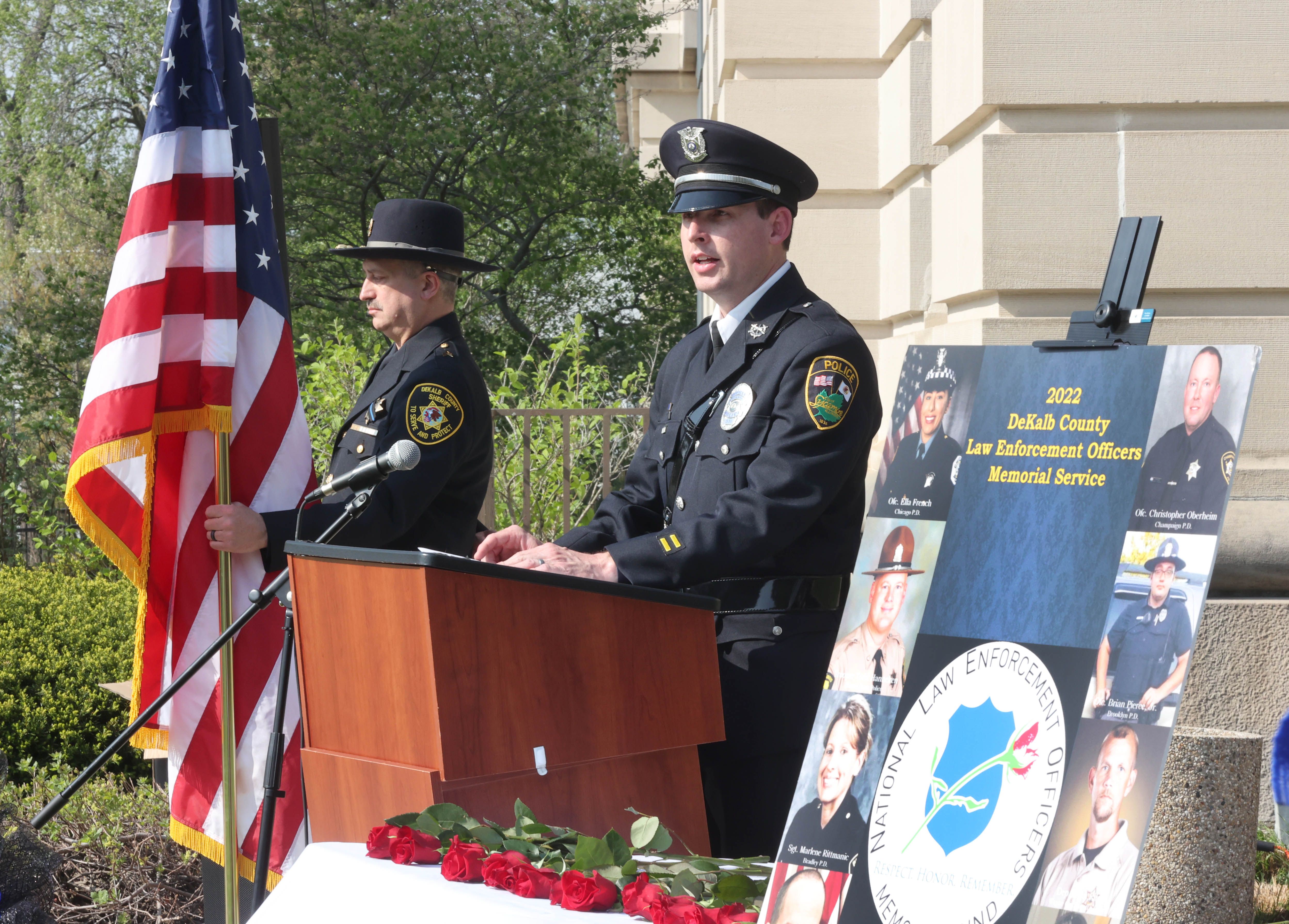 Sycamore Police Detective Ryan Hooper speaks as honor guard member DeKalb County Sheriff Sergeant Tim Duda holds the flag Friday, May 13, 2022, during the DeKalb County Law Enforcement Officers' Memorial Service on the lawn of the DeKalb County Courthouse in Sycamore.