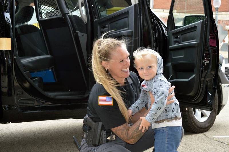 Mt. Morris police officer Cassie Rogers prepares to pick up Logan LeFevre, 2, of Mt. Morris, on Tuesday, Aug. 6, 2024, during the village's first National Night Out.