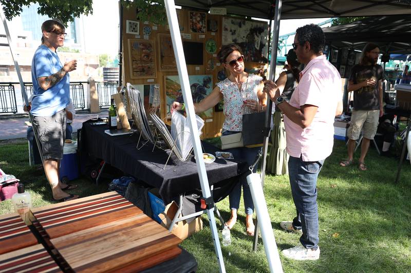Michelle and Nelson Rodriguez look through art for sale at one of the tents at the Wine, Jazz and Arts Fest at Bicentennial Park in Joliet on Saturday, Aug. 19, 2023.