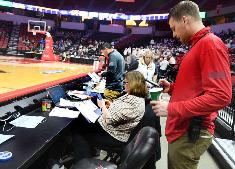 Illinois State University Director of Game Operations Alex Cain, who was the event manager for the girls state basketball finals, checks a text message as he stands behind IHSA Assistant Executive Director Beth Sauser between games on March 2.
