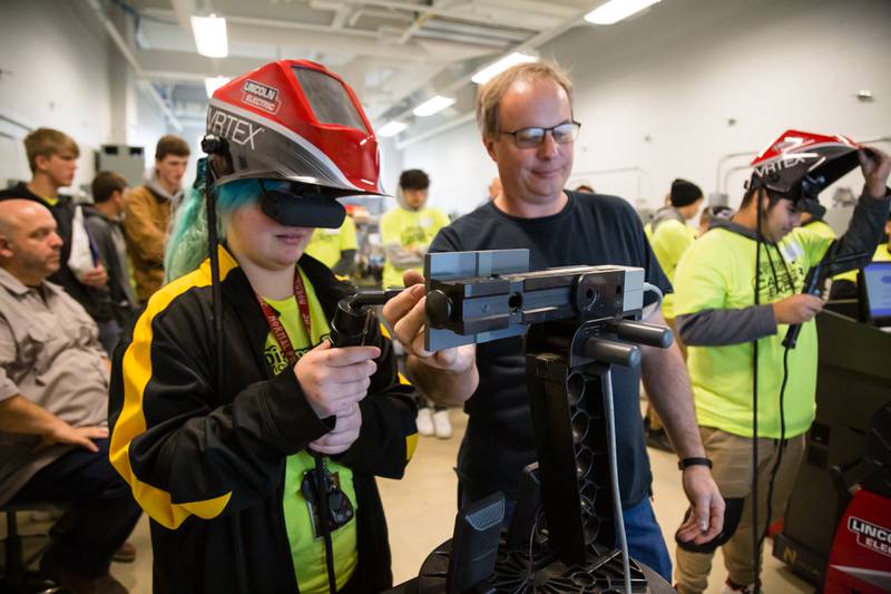 Illinois Valley Community College welding program coordinator Tony Sondgeroth (right) assists a student operating a virtual welder at the 2019 Discover Manufacturing Career Expo.