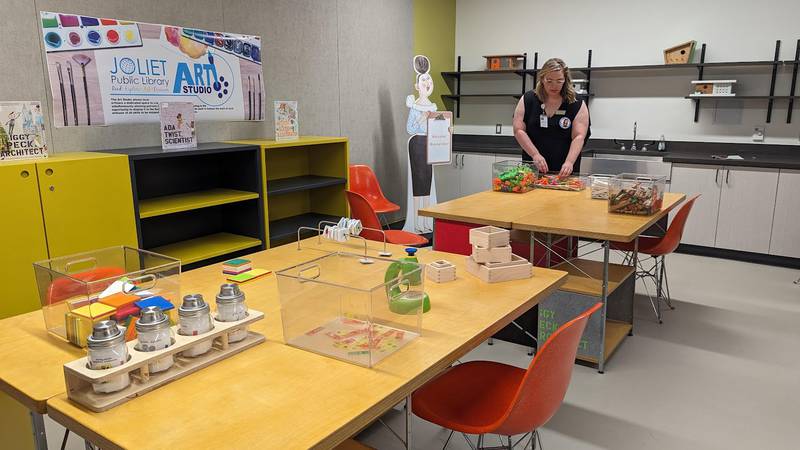 Mallory Hewlett, communications manager at the Joliet Public Library, stands inside “Miss Lila Greer’s classroom,” which is featured in “The Questioneers: Read. Question. Think. PLAY!” exhibit on Wednesday, June 21, 2023. This exhibit is based on the Questioneers book series authored by Andrea Beaty and illustrated by David Roberts. This traveling exhibit featuring the Questioneers characters opened June 16 at the Ottawa Street branch of the Joliet Public Library and is available during library hours through July 29.