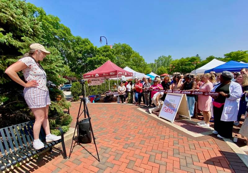 DeKalb Chamber of Commerce membership manager Anna Wilson (left) readies the crowd ahead of a ribbon cutting to celebrate the opening day of the DeKalb farmers market, on Thursday, June 5, 2025, in Van Buer Plaza in downtown DeKalb. The market opened its 30th year Thursday.