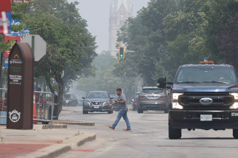 A pedestrian crosses North Chicago Street as haze from the Canadian wildfires hangs over Joliet on Wednesday, June 28th, 2023.