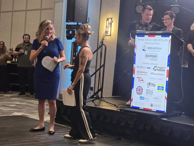 Laura Charland, Shorewood HUGS co-founder (right) honors Peggy Hogan of Marian for Hogan and Marian's longtime support at the Shorewood HUGS' "Lovely London: A Big Ben Bash" 2026 chocolate ball fundraiser on Saturday, Feb. 7, 2026, at Hollywood Casino Joliet. Emcees Roy Gregory and State Rep. Natalie Manley, D-Joliet are seen to the right.