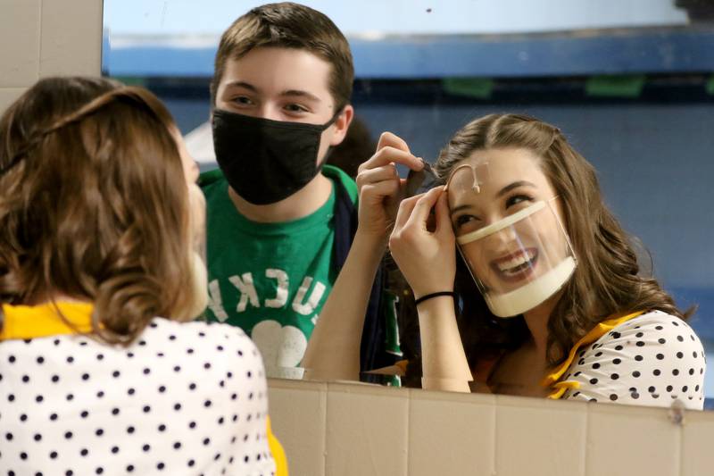 Natalie Virgil, right, laughs as she fixes her microphone to her forehead with lighting head Kendrick Flanigan, both juniors, backstage during a rehearsal Wednesday, March 17, 2021, for the musical "Working" at Crystal Lake Central High School in Crystal Lake.  Each participant in the production is allowed two members of their same household to come view two additional rehearsals at the school, as no tickets will be sold for an official performance due to COVID-19 restrictions.