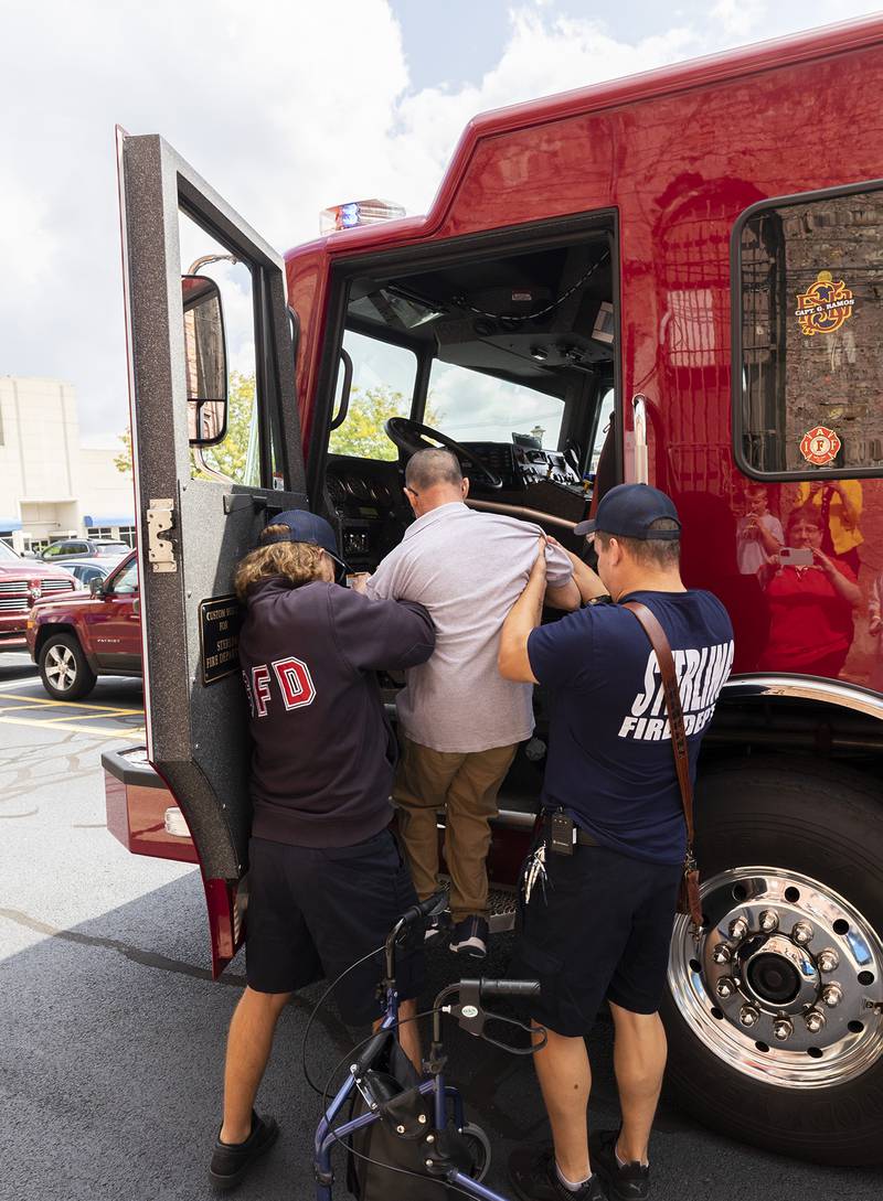 Sterling firefighters Nick Hammer (left) and Eric Behrens help Merlin into the cab of the firetruck Sunday, Sept. 17, 2023. The department, Merlin’s favorite spot to visit, brought a truck in as a surprise for his birthday.