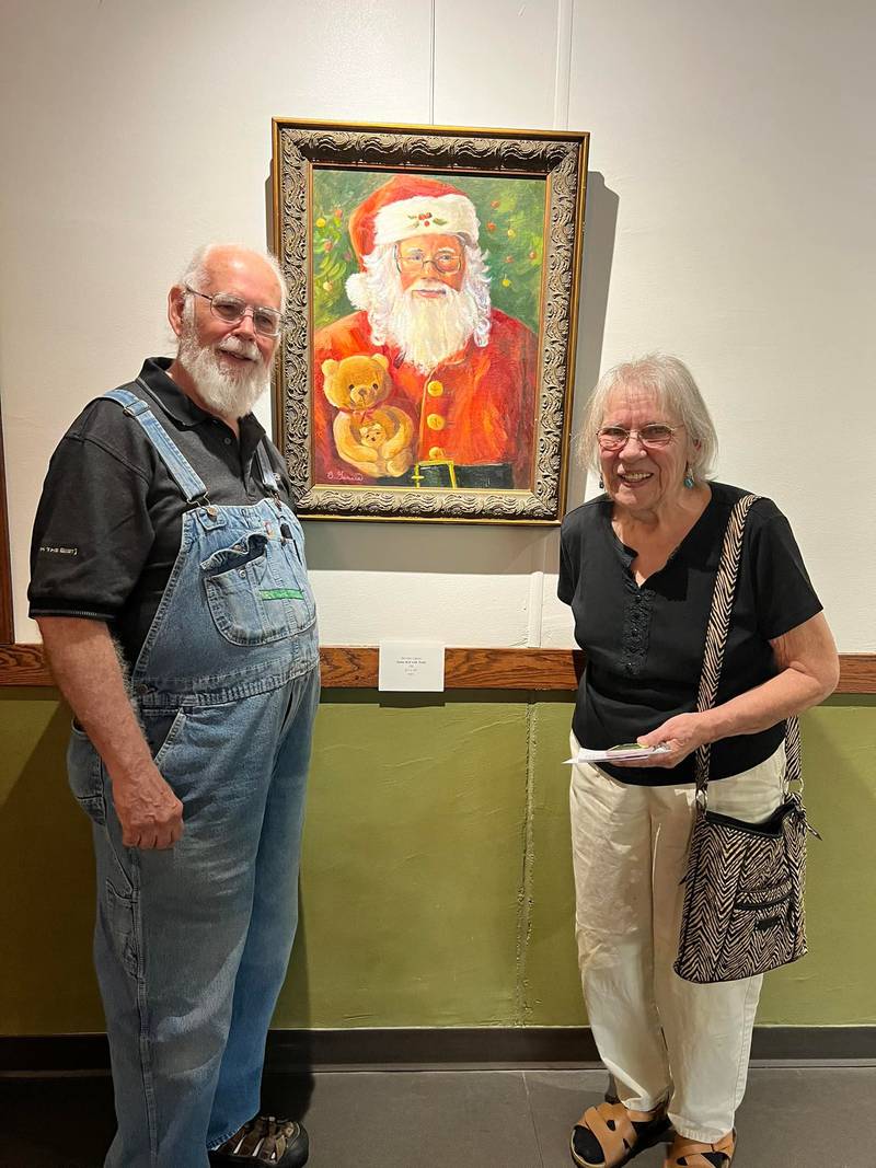 Photographer Bob Logsdon (left) poses with artist Beverly Garcia in front of her holiday depiction of Logsdon, “Santa Bob with Teddy.”