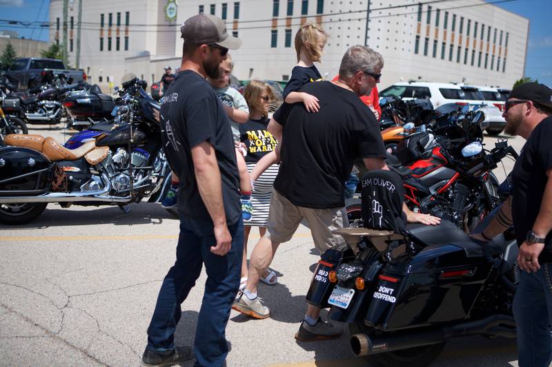 Nathan Olinger (left) holds son Oilver Olinger, 2, with family as they look at dozens of motorcycles parked outside Sycamore Public Library on Sunday, June 22, 2025. The motorcyclists and law enforcement helped escort Oliver, a motorcycle enthusiast, to St. Charles Motorcycle Museum to celebrate his cancer remission.