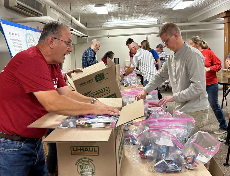 Lane Schurr of the Evangelical Free Church of Mt. Morris and a Serenity Hospice volunteer fill boxes with care packages to be mailed to sailors on the USS Fitzgerald on Thursday, Oct. 16, 2025. Volunteers gathered in the church's basement to assemble the packages.