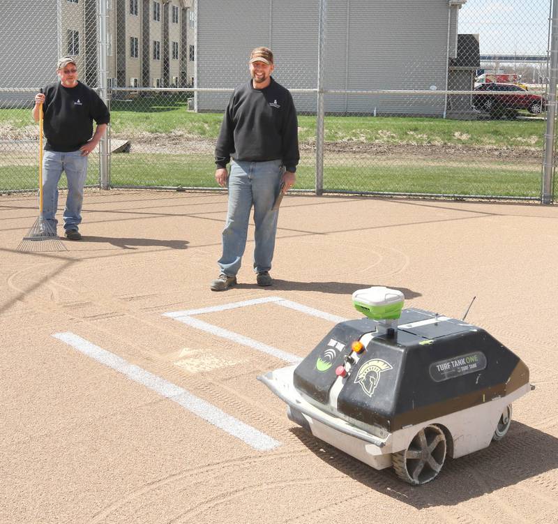 Dane Shaw (left) and Nik Vinz, maintenance for Sycamore Community School District 427, use a robot to line the softball field Tuesday, April 11, 2023, for that nights game at Sycamore High School.