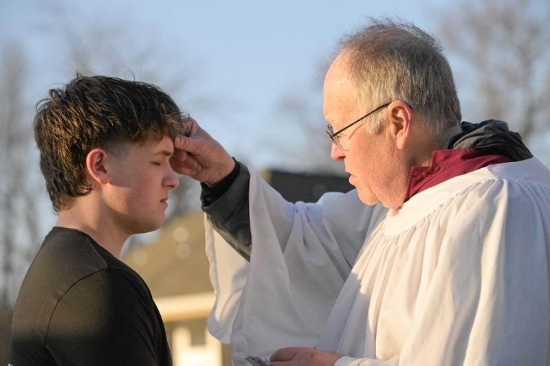 Will Wojtyla of Batavia receives a traditional blessing of a cross of ash on his forehead from Bo Smith of St. Charles Episcopal Church at the Geneva train station on Wednesday, Feb 18, 2026 in Geneva.