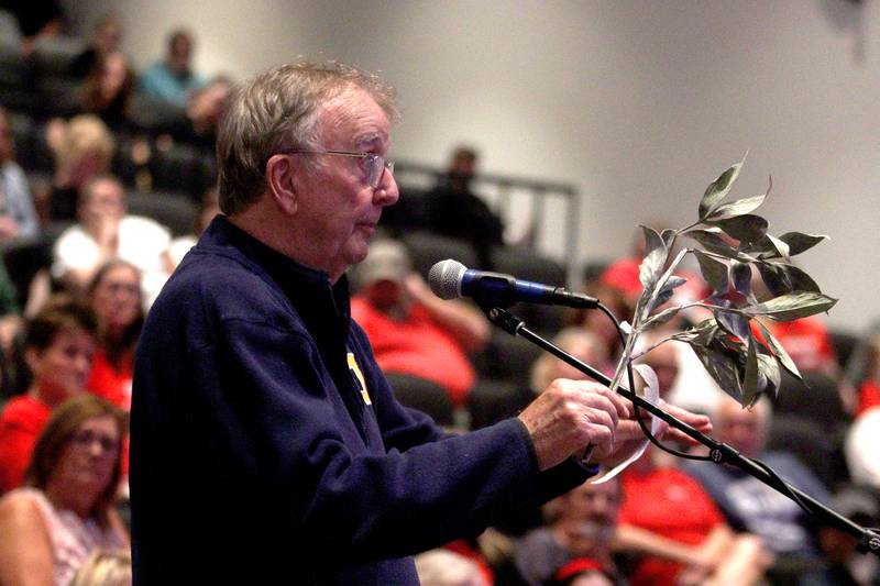 Glen Reid of McHenry waves a dust-covered peony branch from his yard as he speaks against a Jack Pease proposal to mine 110 acres at Route 120 and Chapel Hill Road as the McHenry City Council met on Monday, Aug. 7, 2023, at McHenry High School’s Upper Campus auditorium. Reid’s house lies 150 yards from a gravel pit and he brought the branch to display what he describes as a thick film of dust adversely affecting the foliage.
