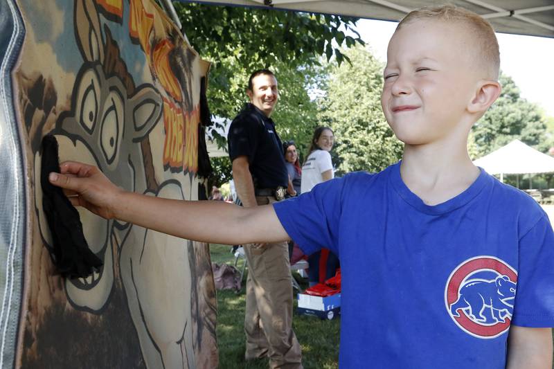 Officer Jeff Diamond, back, watches as Maksym Grudek, 6, of Carpentersville, tries to pin a tail on the donkey during a National Night Out event behind the Algonquin Area Public Library on Tuesday, Aug. 3, 2021, in Algonquin.  The nationwide event brings law enforcement personnel and the community together.