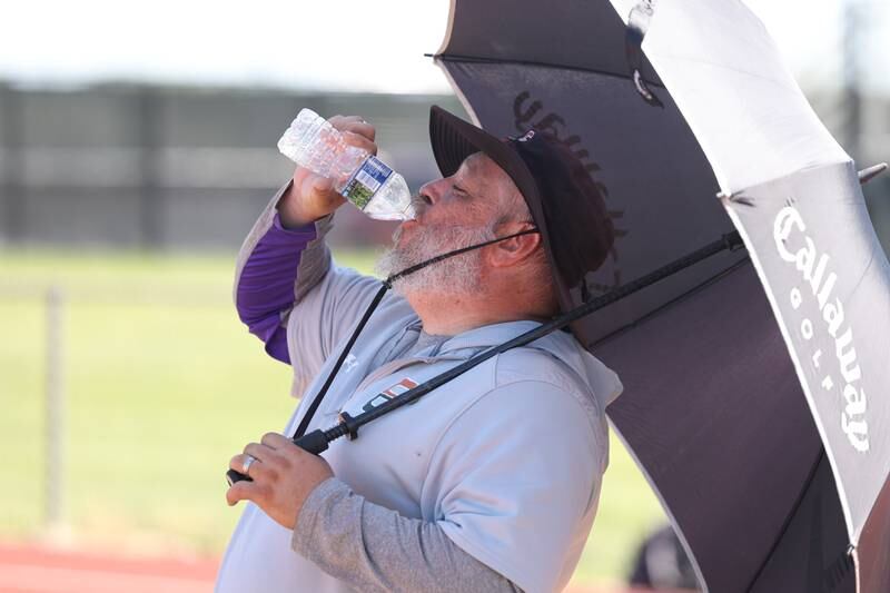 Plainfield East coach Matthew Kee uses an umbrella to blocks out the sun while drinking water during 7-on-7 drills at Lincoln-Way Central. Thursday, June 16, 2022 in New Lenox.