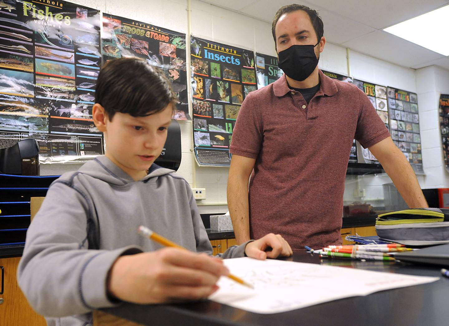 Science teacher Brian Sanford talks with student, Morgan Smith, 13, on Tuesday, March 22, 2022, as he teaches seventh-grade science at Algonquin Middle School. Sanford, who brings his art and games into the classroom to help teach science, has asked students to draw monster movie posters for a science study unit.