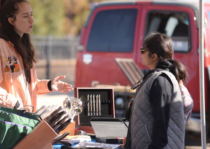 Alyssa Trausch of Elk Grove Village discusses her knifes with Nazia Babul of Glen Ellyn during the last day of the Glen Ellyn French Market Sunday, Oct. 20, 2024.