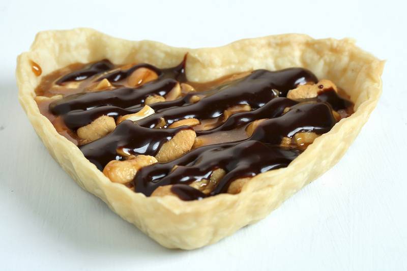 Homemade caramel stars in tartlets for Valentine's Day. Cashews are mixed into the caramel, which is then poured into tart shells. A generous drizzle of chocolate finishes it off.