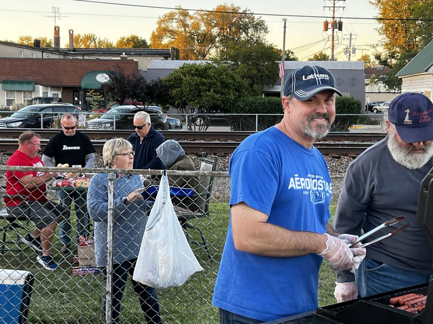 Sandwich City Council members volunteering at the Taste of Sandwich. (At the grill from left to right: Mayor Todd Latham and Alderman Bill Fritsch) (Beyond the fence from left to right: Alderpersons Rich Robinson, Bill Littlebrant, Cara Killey and Rick Whitecotton)