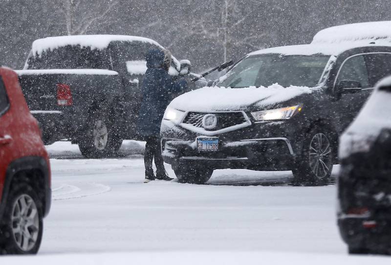 A woman removes snow and ice from a vehicle in the parking lot of McHenry County Government Center in Woodstock, as a winter storm moves through McHenry County on Tuesday, Jan. 9, 2024, delivering snow to most of the county.