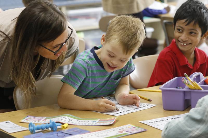 Teacher Jessica Weglarz checks in with Cody Binger, a first grader with Down syndrome, as he works on a class assignment about community helpers, Wednesday, Sept. 14, 2022, at Leggee Elementary School in Huntley. Binger will appear in a national video seeking to raise awareness for Down syndrome set to be shown in Times Square on Saturday, Sept. 17. The video will include 500 adults and children with Down syndrome.