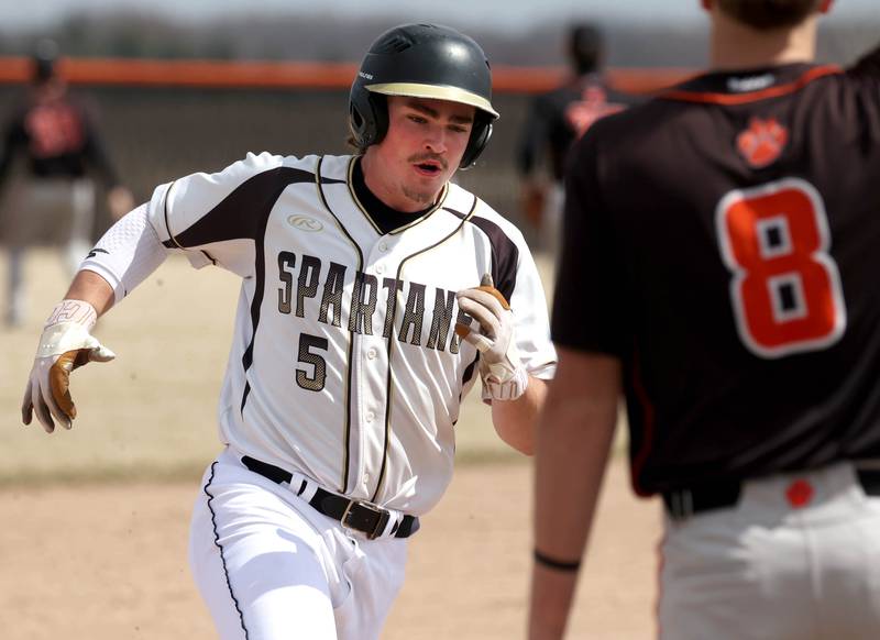 Sycamore's Tyler Lojko rounds third past Byron’s Cooper Mershon on his way to scoring a run during their game Wednesday, March 26, 2025, at DeKalb High School. Sycamore’s home field was damaged in last week’s storms so today’s game was played on DeKalb’s field.