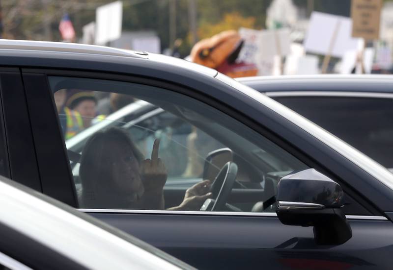 A woman gives the crowd the finger while stopped at a traffic light during a "No Kings” protest rally on Saturday, Oct. 18, 2025, along Route 31 in McHenry. The protest drew thousands of protesters to the area to protest the policies of President Donald Trump.