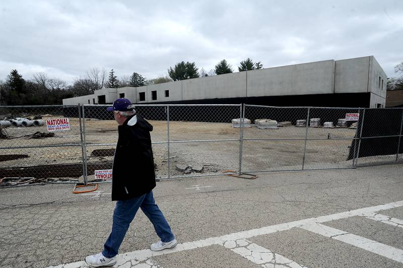 A man walks past the foundation walls of a five-story, 100-unit apartment building in downtown Fox River Grove on May 2, 2022, Work has stopped on the building after developers received a demolition permit in August and a limited permit in November that allowed the construction of footings for the building and foundation walls. That work is now complete and work cannot continue until the village signs off on the final plans.