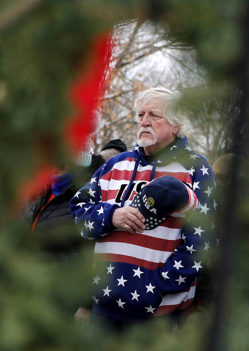 Gary Snell is framed by a wreath as he listens to a prayer during McHenry's Wreath Laying Ceremony in honor of fallen veterans on Friday, Dec. 5, 2025, at St. Mary's Catholic Cemetery in McHenry. The event was hosted by McHenry American Legion Post 491 and Team Home Depot.