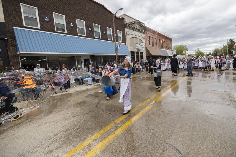 A youngster tosses a bucket of water onto the streets of Fulton Saturday, May 3, 2025, as the traditional cleaning of the parade route takes place during Fulton’s Dutch Days.