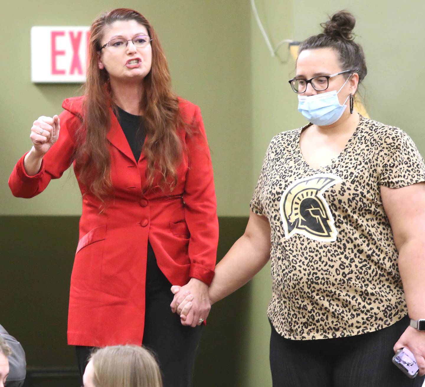 Community members Diana Hulst (left) and Liz Lundeen, who attended the Sycamore District 427 school board meeting to support teachers, asks people to put on masks so the meeting could start Tuesday, Feb. 8, 2022, at Sycamore High School. Despite most of the attendees wearing masks, the meeting was still halted and switched to a virtual format after School Board President Jim Dombeck said several maskless individuals refused to comply with districts instruction to wear a face covering.