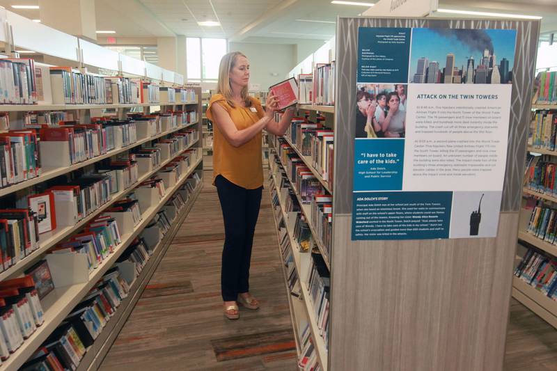 Nami Quaranta, of Lindenhurst, learning & development coordinator, puts away an audiobook close to a 9/11 poster on display to commemorate the 20th Anniversary of 9/11 at the Lake Villa District Library in Lindenhurst. Fourteen 9/11 posters are on display which came from the 9/11 National Memorial & Museum  in New York. (9/7/21)