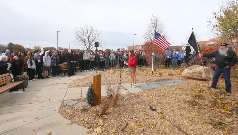 Ella Sartain, a senior at Hall High School, reads the names of all 24 veterans who attended Hall High School that died during WWII during the Veterans Day re-dedication on Tuesday, Nov. 11, 2025 in the Hall High School auditorium. Sartain is the second scout to dedicate her Eagle service project to the 24 fallen soldiers. She started with the 24 names on Kim Cabodi's boulder and hoped to find a pictures of each soldier and biography information to make a plaques for each tree.  She met with her U.S. History teacher, Ms. Carpenter, who helped her throughout the project, including organizing the Hall teachers to bake items in the foods lab to raise bake sale money at her Rip's Chicken fundraiser. 

As Ella started her research, she soon realized that this task was harder than she initially thought. There was not much information or photos readily available. Ella reached out to the community on Facebook asking for information.  171 shares later, she started to connect with family members who had stories and photos to share. She also traveled to area libraries in Ladd, Cherry, and Spring Valley and found newspaper clippings, town historical books, and helpful librarians. She contacted the Spring Valley and Ladd American Legions, who were also eager to assist. Eventually, with a lot of footwork, emails, phone calls, and networking, Ella was able to find a picture for each man as well as his story. Many of the people and family members who heard about the project offered to donate as well. Ella raised above her initial goal and was able to  break ground. She worked with Graphic Electronics in Spring Valley to design the plaques and her scout troop to build the posts. She also had wreath hooks specially designed by metal worker and blacksmith, Jason Joiner. With her extra funds, Ella worked with landscape architect Cara Finney to design a new garden area to enhance the rock. She placed a flagstone path from the existing sidewalk to the rock and purchased two additional benches for the park. A 25th post near the rock has a QR code to this site. Mr. Van Fleet, the tech coordinator at Hall, helped Ella to create this website where all of the information she gathered could be stored. In 2025, the WWII Memorial Park, now on the east side of Hall's campus, got some fresh landscaping and plaque markers for each tree, along with this website, to continue the tribute to the 24 fallen soldiers. These were all part of Ella Sartain's Eagle Scout Service Project.