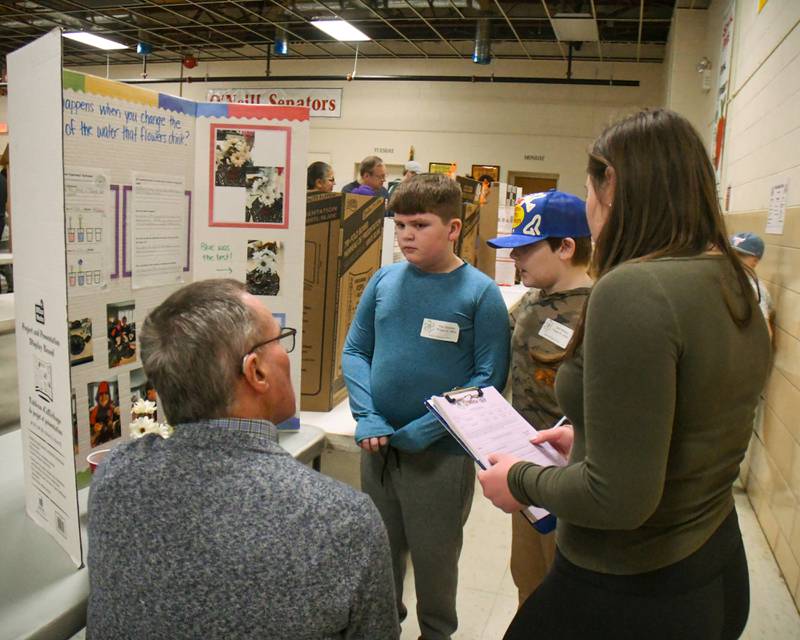 Students Max Beesley, left, and Jack Molitor, talk with judges Jeff Dillon and Vivian Mitropoulos about their project on changing the color of water in flowers on Saturday Jan. 25, 2025, during the Downers Grove District 58 science fair held at O’Neill Middle School.