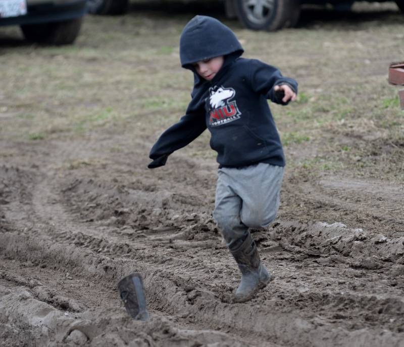 Bruce Larson, 5, of Dixon, hops back over ruts in mud in an attempt to retrieve his boot while playing in the mud at the Hazelhurst Spring Consignment Auction on Saturday, April 5, 2025.. Bryce's dad, Zach, was able to pull the boot from the mud.