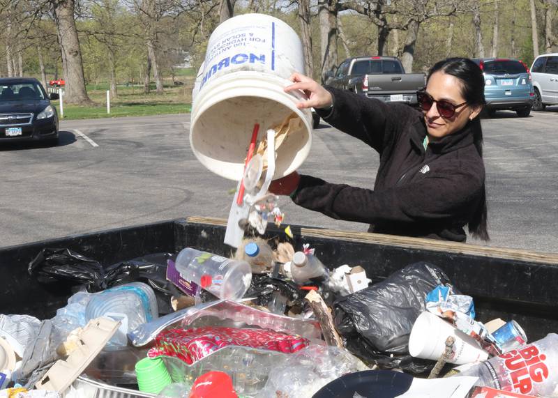 Jovanna Ponce, from Sycamore, pours the trash she collected into the trailer being used as a dumpster Monday, April 22, 2024, during an Earth Day Clean Up event at Hopkins Park in DeKalb.