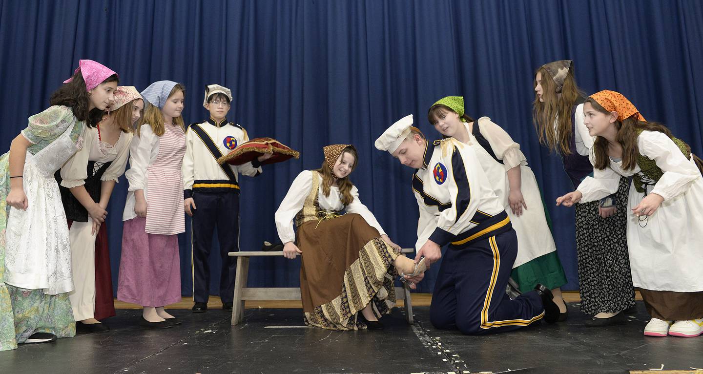 The cast of "Cinderella" looks on as various members try on the slipper in a scene from the musical performed by Marquette Academy students.