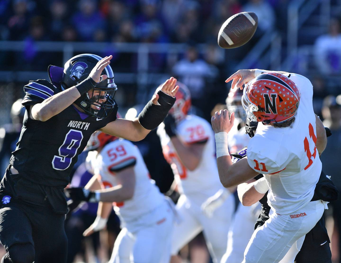 Normal Community quarterback Kyle Beaty (11) has the ball jarred loose by Downers Grove North's Joe Edwards (hidden behind Beaty) as North's Jimmy Janicki (9) pressures from the front during an IHSA Class 7A semifinal game on Nov. 18, 2023 at Downers Grove North High School in Downers Grove .